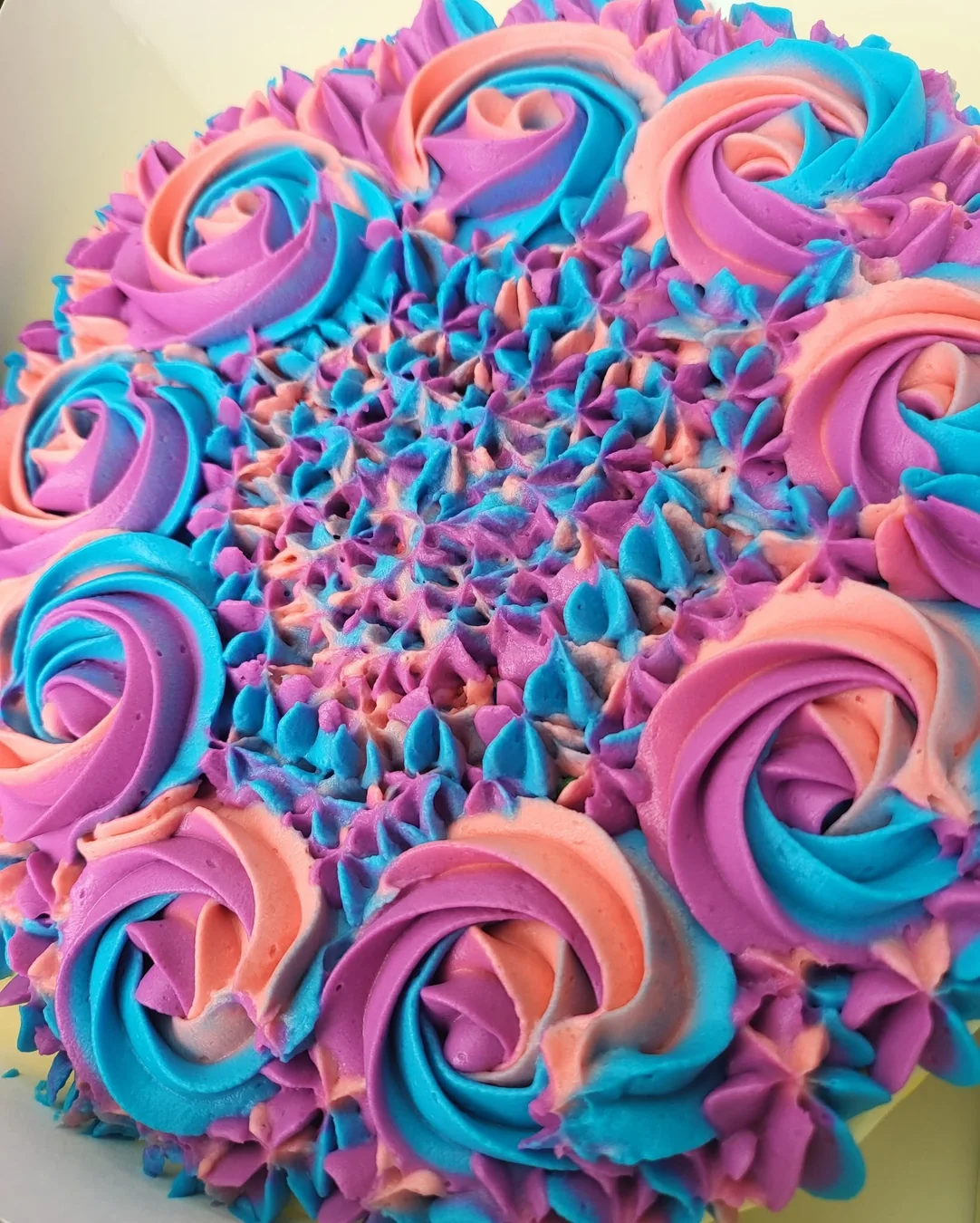 Bright pink, purple and blue buttercream roses topping a whole cheesecake