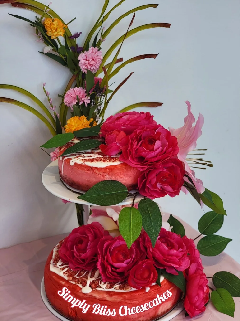 Two-tier display of pink celebration cheesecakes adorned with flowers